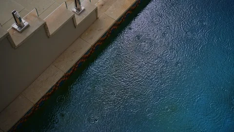 Light rain drops fall on vivid blue swimming pool surface next to steps. Stock Footage 125370019