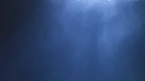 Light rays pierce the blue water, illuminating bubbles and particles, with .. Stock Footage 293463011