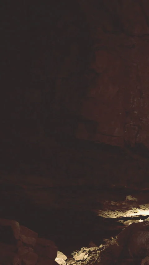 Light shines into dark cave revealing rock formations and shadows Stock Footage 331763580