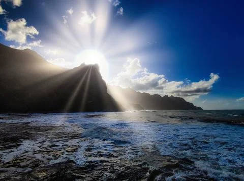Light shines through mountains at sunset over the ocean Stock Photos