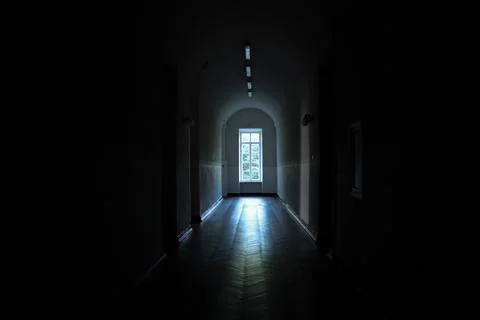 Light shines through an open door at the end of a dark hallway in a quiet Stock Photos