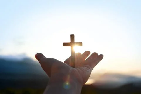 Light shining between the hands outstretched toward the sun and the cross Stock Photos
