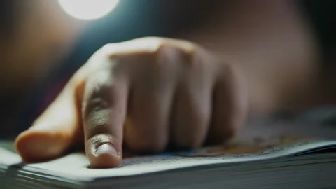 Light shining on a person's hand pointing at text in a book Stock Footage 275296734