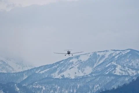 Light single-engine airplane climbing over snow-capped mountains Stock Photos