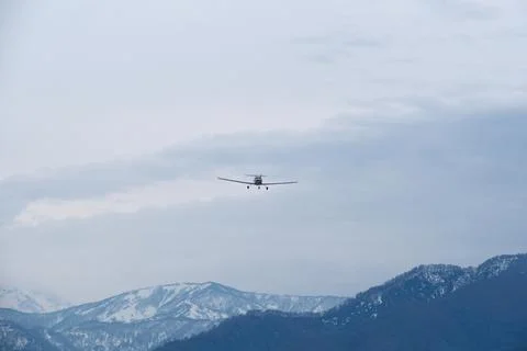 Light single-engine airplane climbing over snow-capped mountains Stock Photos