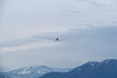 Light single-engine airplane climbing over snow-capped mountains Stock Photos