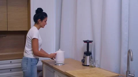 A light-skinned brunette in the middle ground approaches the table with a kettle Stock Footage 263183927