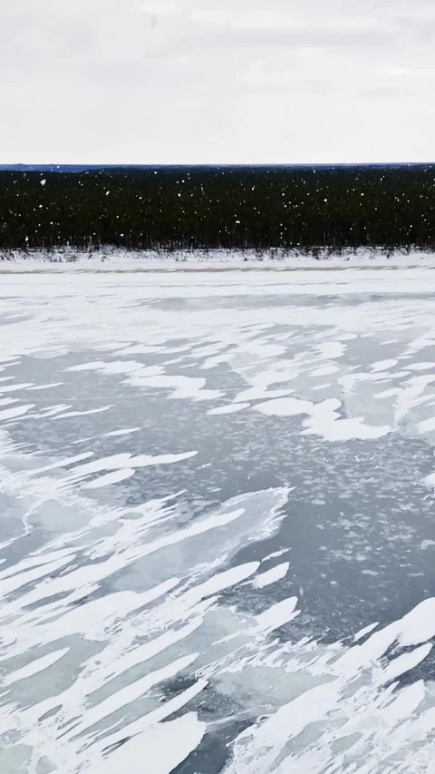 Light snow falls over a grey glazed frozen bay with scattered snow patches Stock Footage 332457044