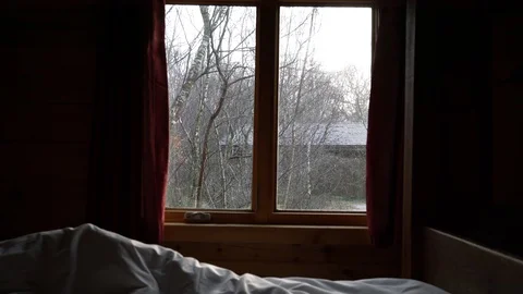 Light snowfall can be seen through a window in front of an unmade bed, 4k, UK Stock Footage 86487837