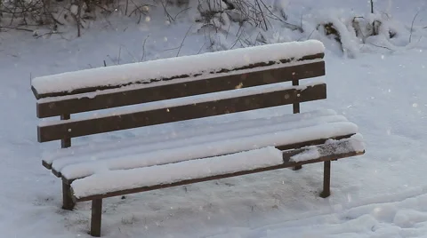 Light snowfall in cold winter day and empty bench covered with snow in the park. Stock Footage 59216044