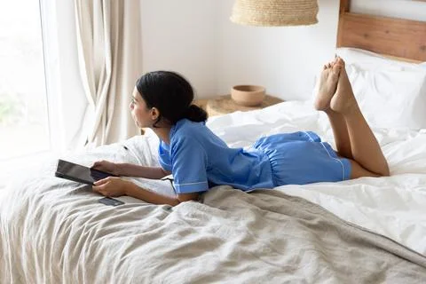 Light streaming through curtains illuminating tablet resting on white bed linens Stock Photos