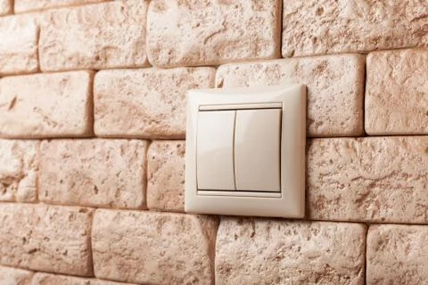 Light switch on a beige brick wall. Stock Photos