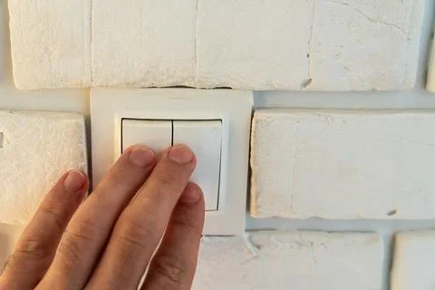Light switch being pressed by hand on white painted brick wall, dual button Stock Photos