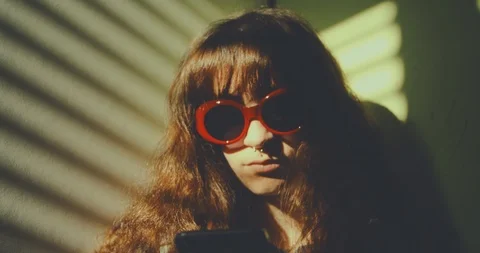 Light through window blinds frame a pierced girl wearing red sunglasses while su Stock Footage 87467010