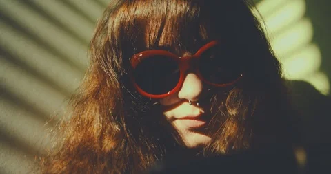 Light through window blinds frame a pierced girl wearing red sunglasses while su Stock Footage 87467374