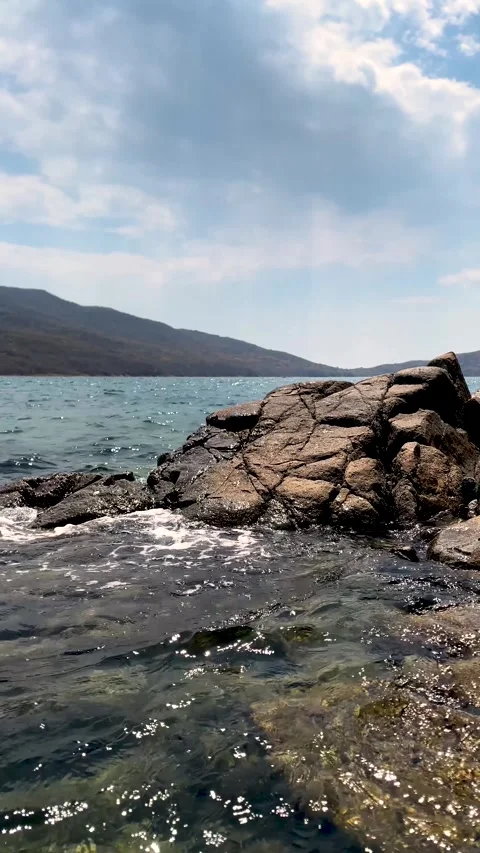 Light wave crashes against rocky shore of sea. Glistening splashes in sunshine. Stock Footage 309732790