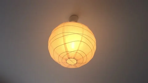 A light in an white and round paper-lampshade getting switched on and off Stock Footage 167754744