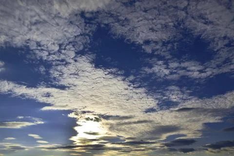 Light white clouds in the summer blue sky are illuminated by the bright sun b Stock Photos