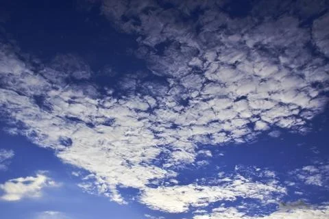 Light white clouds in the summer blue sky are illuminated by the bright sun b Stock Photos