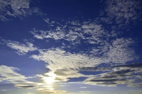 Light white clouds in the summer blue sky are illuminated by the bright sun b Stock Photos