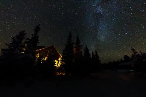 Light from the window of a forest hut under the night sky of the milky way in Stock Photos