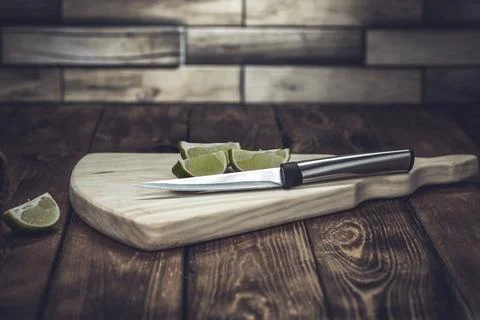 Light wood cutting board with a knife and pieces of lime on a wooden table Stock Photos
