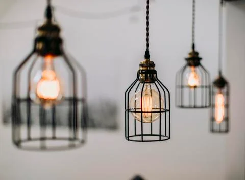 Lightbulbs protected by wire hang in front of a white wall inside Stock Photos