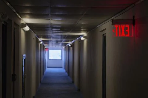 Lighted glowing red emergency exit signs in hallway with arrows pointing the way Stock Photos