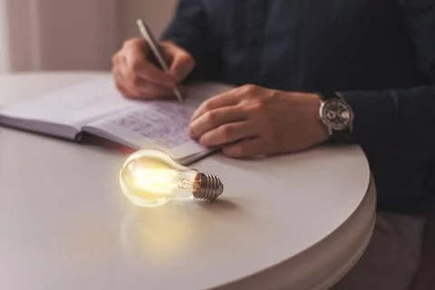 Lighted light bulb lies on a table near a writing business man idea, innovati Stock Photos