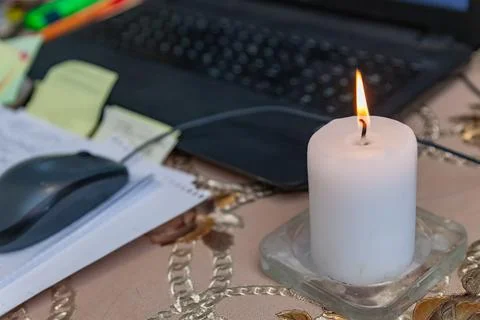 A lighted white candle, a computer mouse, writing sheets, the edge of a lapto Stock Photos