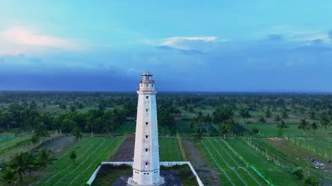 Lighthouse above green fields beneath blue evening sky Stock Footage 335440607