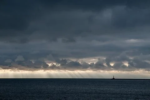 Lighthouse and sun rays over dark calm sea Stock Photos