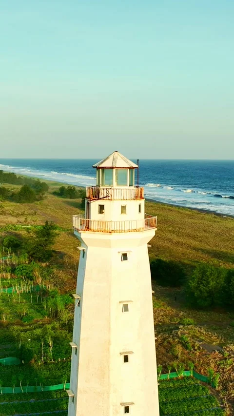 Lighthouse centered above green fields and coastline Vídeo Stock 335432382