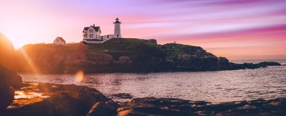 The lighthouse at dawn over the ocean, the sun peaks through Stock Photos