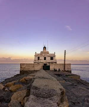 Lighthouse at the edge of the sea at sunset Stock Photos