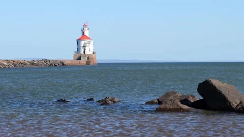 Lighthouse at end of pier and large boulders in shallow blue water. Stock Footage 148170390