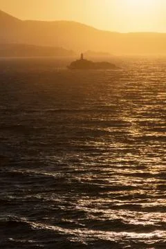Lighthouse on islet at sunset between stormy sea in Greece. Stock Photos