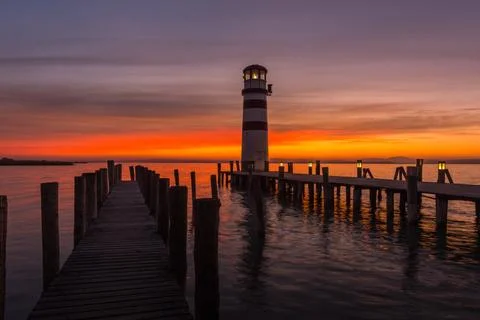 Lighthouse with lantern on a jetty from a lake while sunset Stock Photos