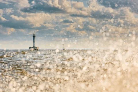 Lighthouse of marine navigation through splashing water at sunset, sailing boat Stock Photos