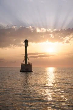 Lighthouse in the Ocean at Sunset with Sun Rays Stock Photos