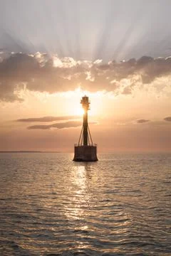 Lighthouse in the Ocean at Sunset with Sun Rays Stock Photos