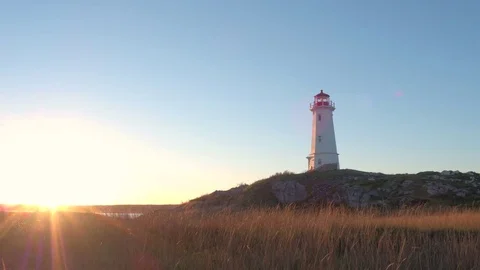Lighthouse with outlook tower standing on grassy seashore at golden light sunset Stock Footage 73723009