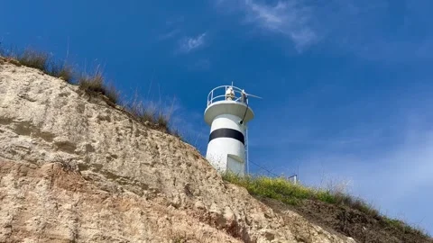 Lighthouse over sandy cliff and blue sky - stock video Stock Footage 240344036