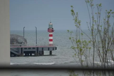 Lighthouse with red and white stripes standing on a concrete pier over the sea, Stock Photos