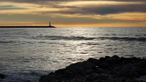 Lighthouse on a rocky pier during sunset with ocean waves and dramatic sky Stock Footage 297611528