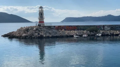 Lighthouse on rocky pier with graffiti, surrounded by calm sea and distant .. Stock Footage 324707309