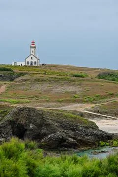 Lighthouse on Rugged Coastal Cliffs Overlooking Calm Sea Under Overcast Sky 写真素材