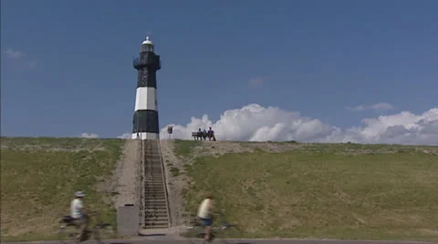Lighthouse + sea dike, cyclists and people sitting on bench Stock Footage 24492184
