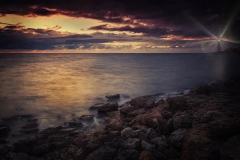Lighthouse on the seashore at night with rays of light Stock Photos