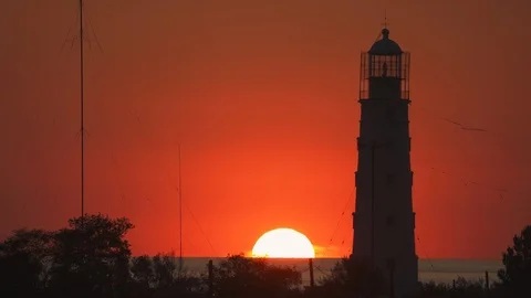 Lighthouse on the shore, the sun goes down in the sea over the horizon Stock Footage 119930655